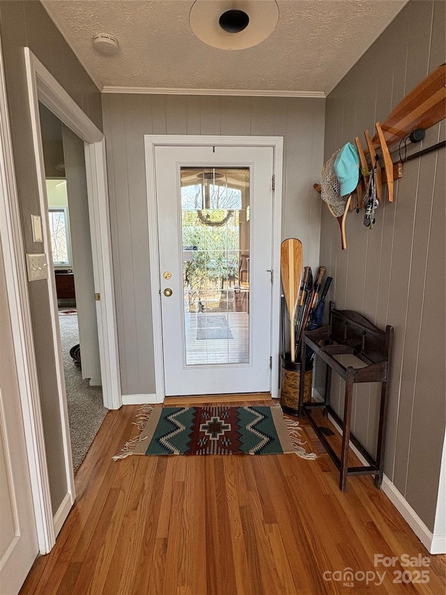 doorway with crown molding, a textured ceiling, and wood finished floors