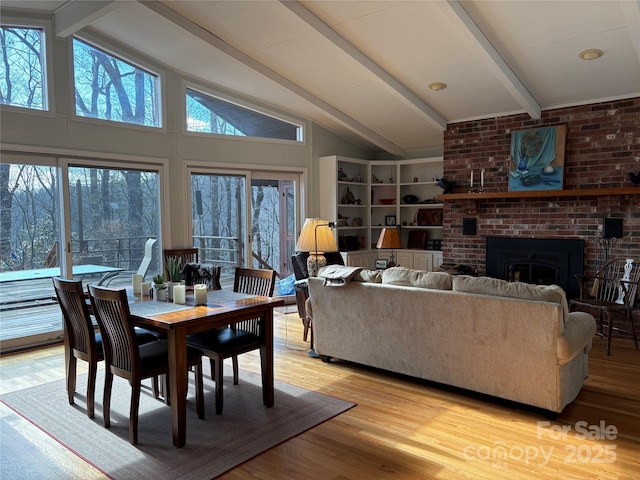 dining area featuring a healthy amount of sunlight, vaulted ceiling with beams, light wood-type flooring, and a fireplace