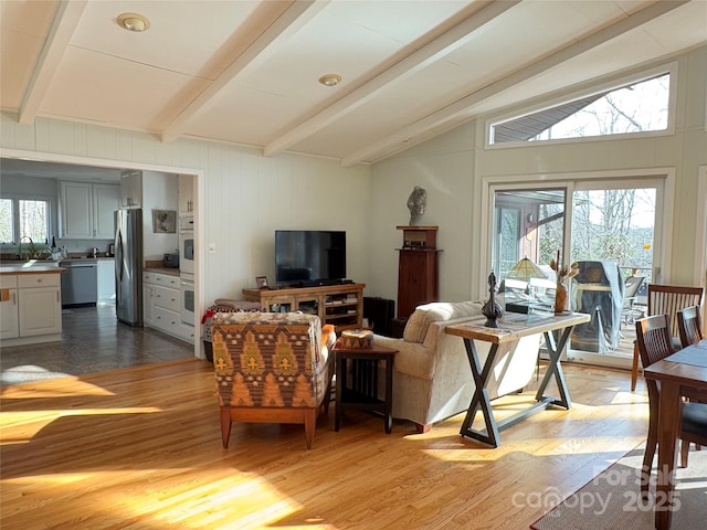 living room with lofted ceiling with beams, plenty of natural light, and light wood-style flooring