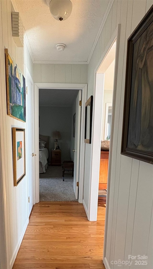 hall featuring a textured ceiling, light wood-style floors, and crown molding