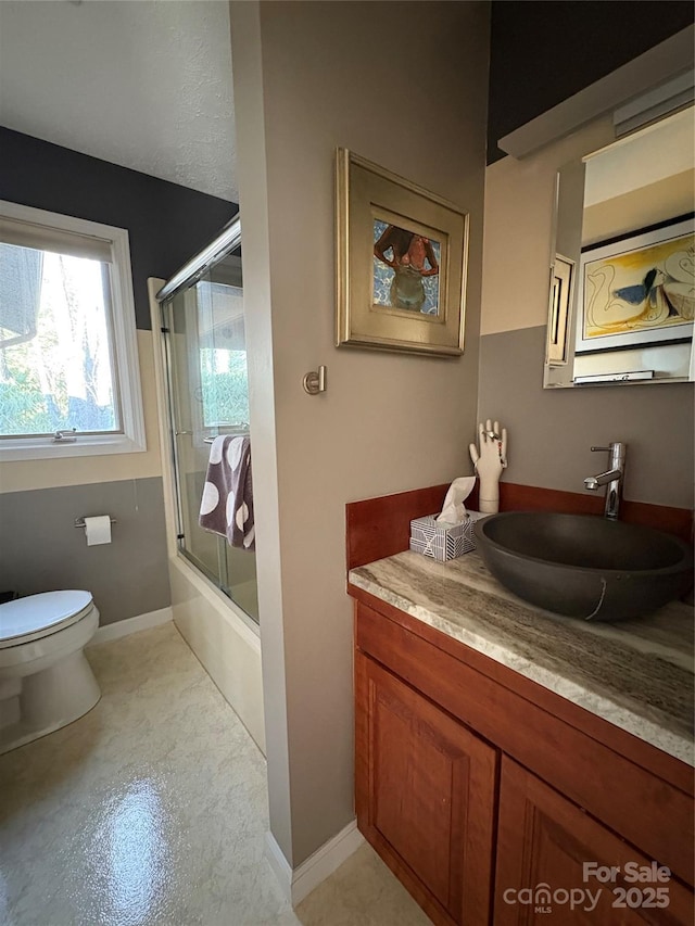 full bathroom featuring toilet, enclosed tub / shower combo, baseboards, and vanity