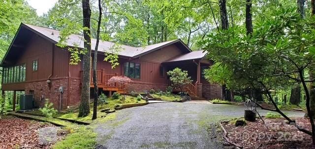 view of side of property featuring stone siding, gravel driveway, and central AC unit