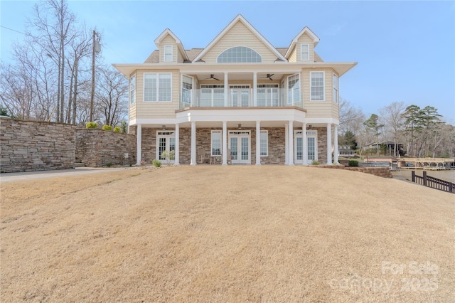 view of front facade featuring a ceiling fan, stone siding, fence, french doors, and a balcony