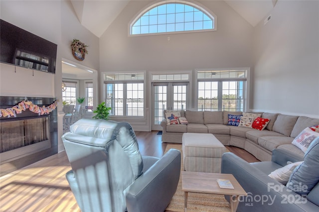 living area featuring a fireplace, light wood-style floors, visible vents, and high vaulted ceiling