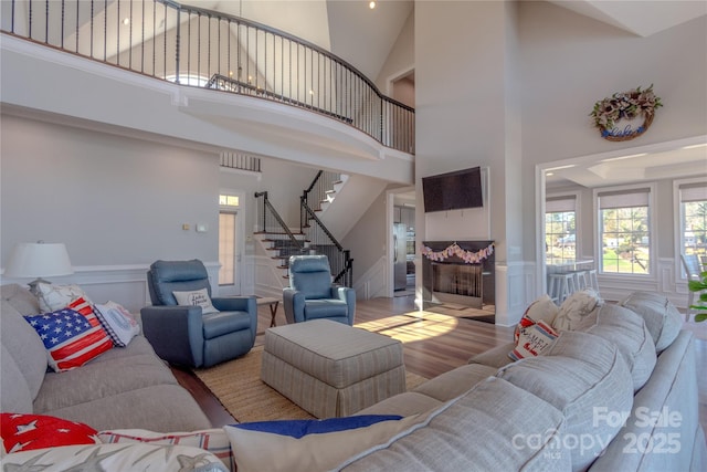 living area with wood finished floors, wainscoting, a decorative wall, a towering ceiling, and stairs