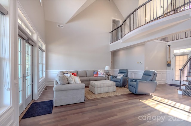 living room featuring visible vents, wood finished floors, stairway, a high ceiling, and wainscoting