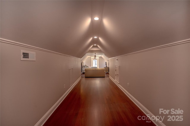 hallway featuring dark wood-type flooring, baseboards, visible vents, and vaulted ceiling