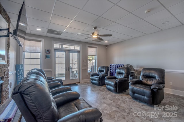 living room featuring a ceiling fan, baseboards, a fireplace, a drop ceiling, and french doors