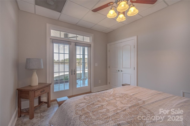 bedroom featuring a water view, french doors, baseboards, a paneled ceiling, and access to exterior