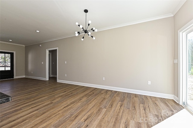 spare room featuring baseboards, ornamental molding, wood finished floors, and a notable chandelier