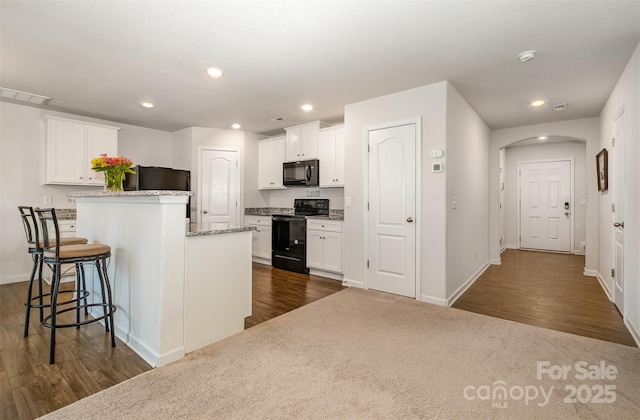 kitchen with recessed lighting, visible vents, white cabinetry, black appliances, and a kitchen bar