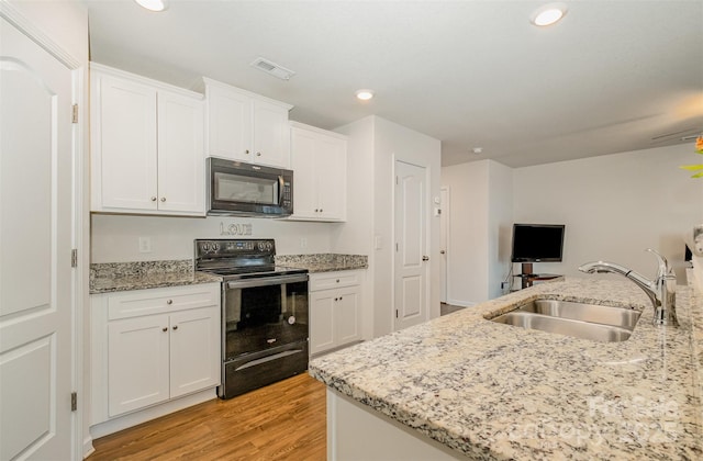 kitchen with visible vents, light wood-style flooring, white cabinets, a sink, and black appliances