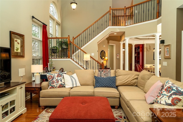 living room with stairway, decorative columns, a towering ceiling, and wood finished floors