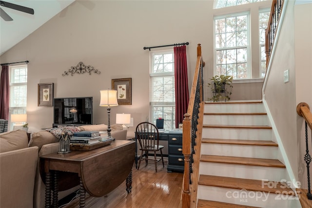 living area featuring stairway, wood finished floors, a ceiling fan, and a healthy amount of sunlight