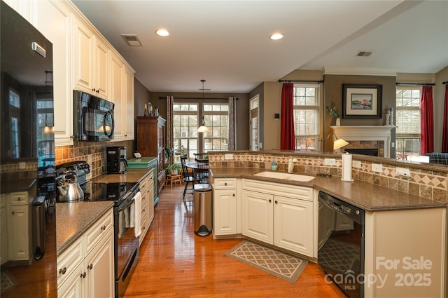 kitchen featuring visible vents, light wood-type flooring, black appliances, a fireplace, and a sink