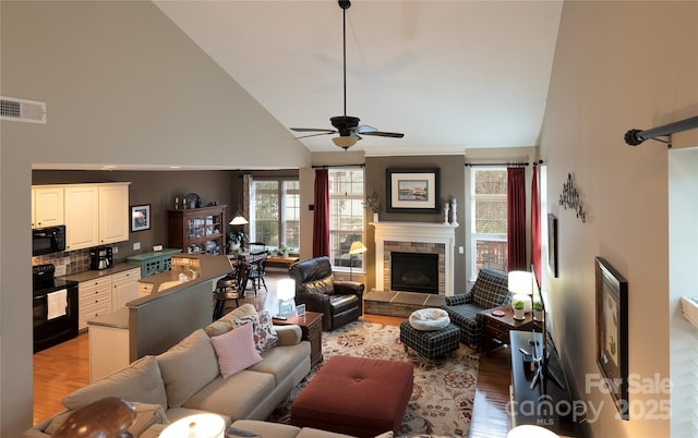 living area with a fireplace, visible vents, a ceiling fan, high vaulted ceiling, and light wood-type flooring