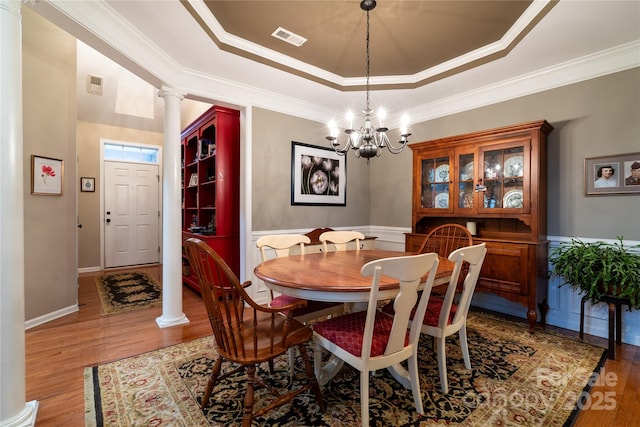 dining room featuring a tray ceiling, visible vents, decorative columns, and wood finished floors