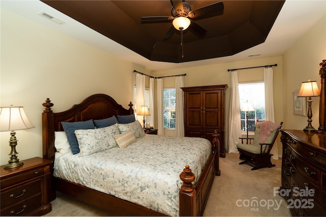 bedroom with a tray ceiling, visible vents, and light colored carpet