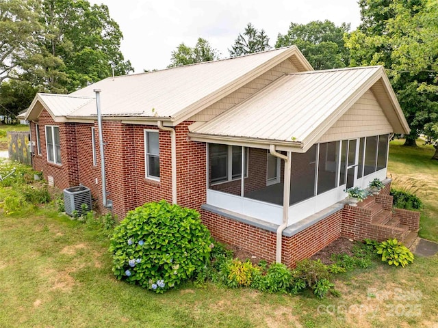 view of side of property featuring central AC unit, a sunroom, metal roof, a yard, and brick siding