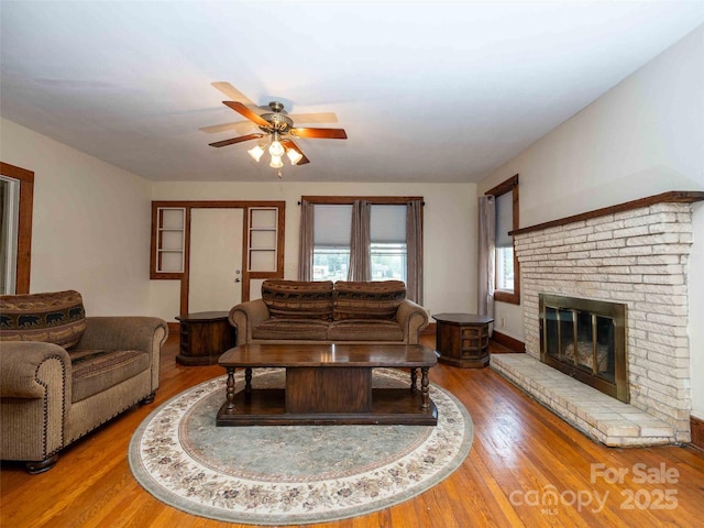 living room featuring a fireplace, a ceiling fan, and wood finished floors