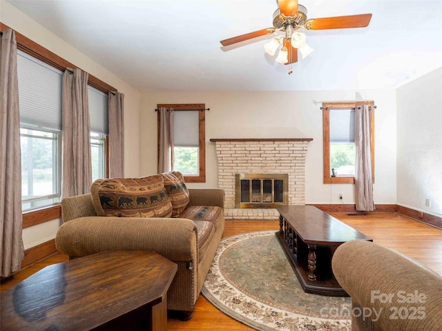 living room with ceiling fan, a fireplace, baseboards, and wood finished floors