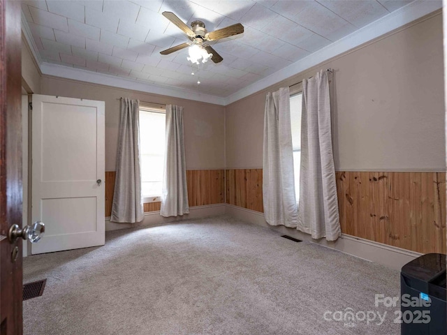 empty room with ornamental molding, wood walls, and wainscoting