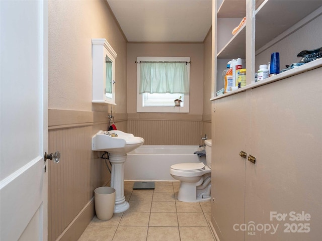 bathroom with a bath, wainscoting, toilet, and tile patterned floors