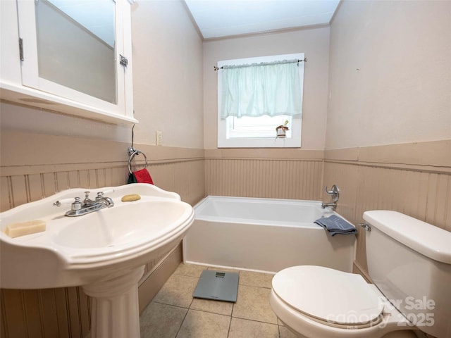 bathroom featuring a tub to relax in, wainscoting, toilet, and tile patterned floors