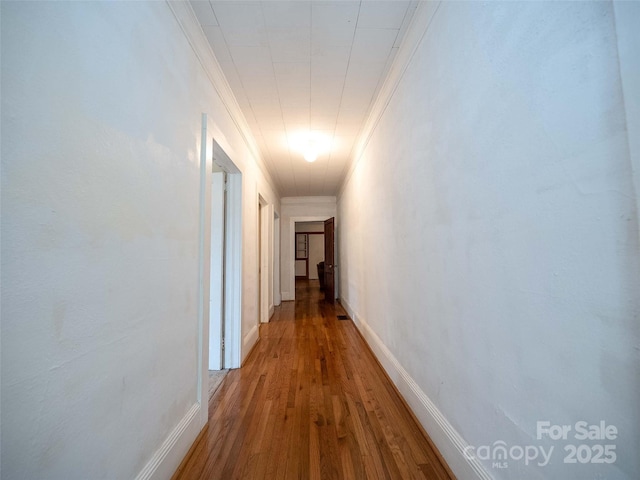 hall featuring ornamental molding, baseboards, and wood finished floors