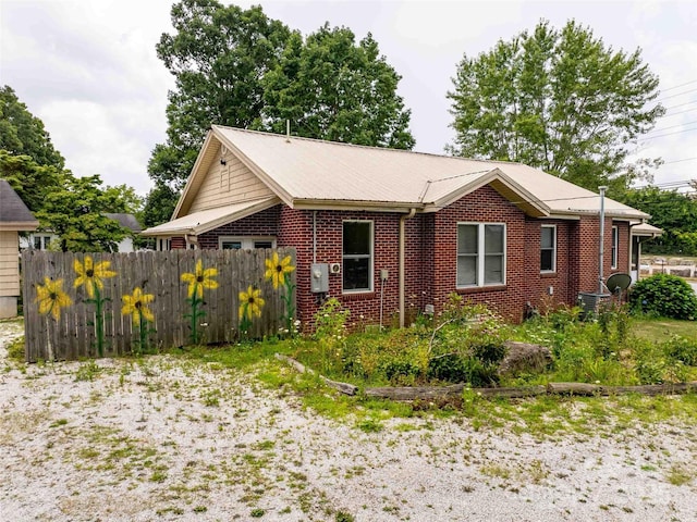 view of property exterior with metal roof, brick siding, and fence