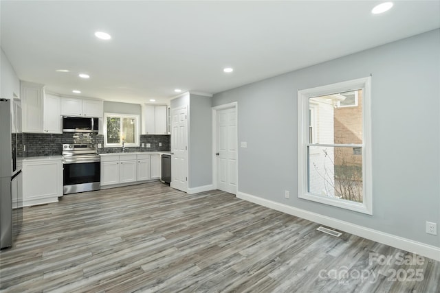 kitchen with baseboards, appliances with stainless steel finishes, white cabinetry, and decorative backsplash