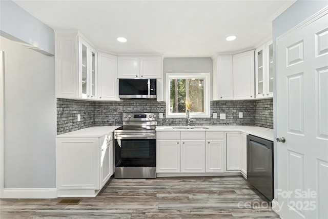 kitchen featuring light countertops, decorative backsplash, appliances with stainless steel finishes, white cabinets, and a sink