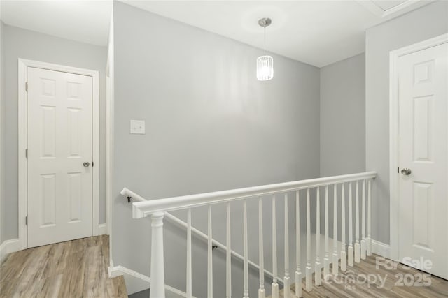 hall with wood finished floors, an upstairs landing, and baseboards