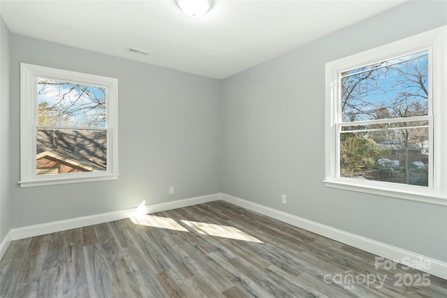 unfurnished bedroom featuring baseboards, multiple windows, visible vents, and wood finished floors