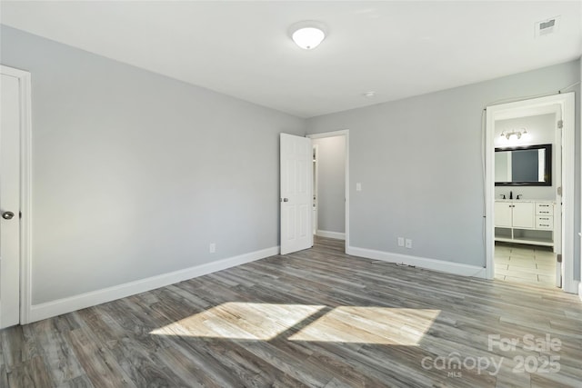 unfurnished bedroom featuring visible vents, a sink, ensuite bath, wood finished floors, and baseboards