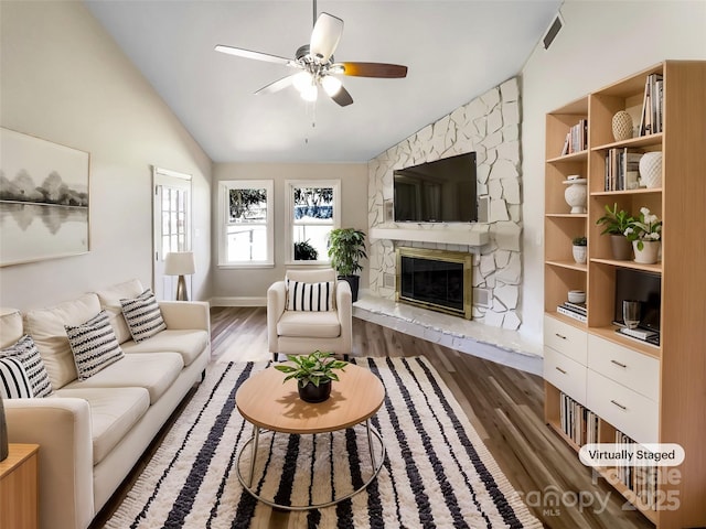 living area featuring lofted ceiling, a stone fireplace, dark wood-type flooring, visible vents, and a ceiling fan