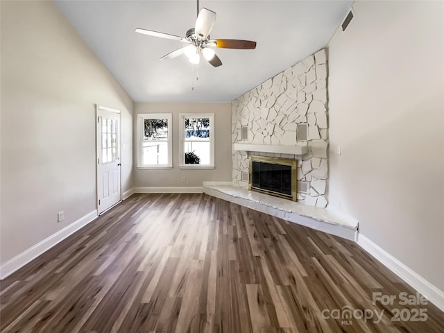 unfurnished living room featuring a ceiling fan, vaulted ceiling, a stone fireplace, and wood finished floors