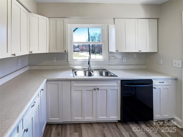 kitchen with black dishwasher, white cabinets, a sink, and light countertops