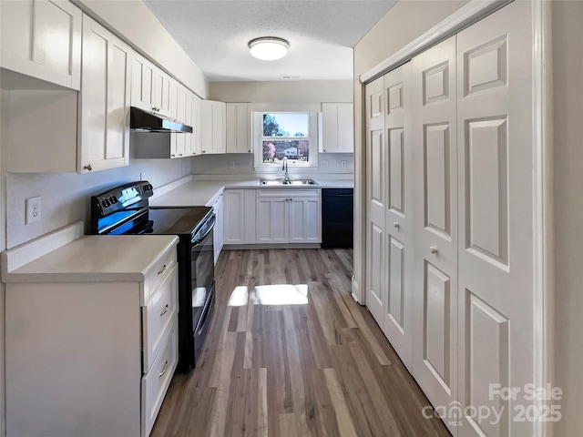 kitchen with under cabinet range hood, light countertops, black appliances, white cabinetry, and a sink