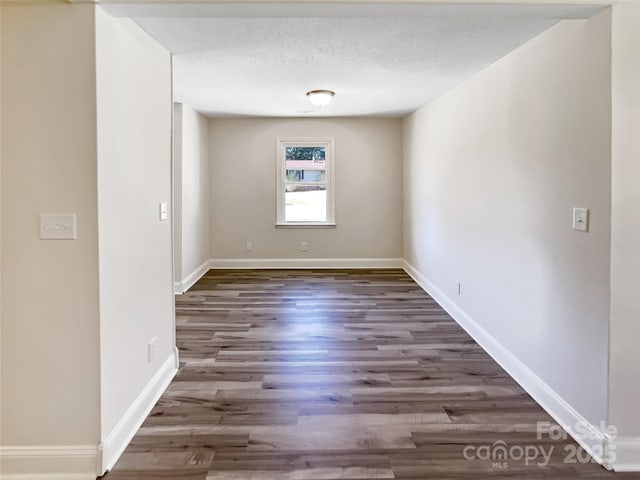 unfurnished room with a textured ceiling, baseboards, and wood finished floors