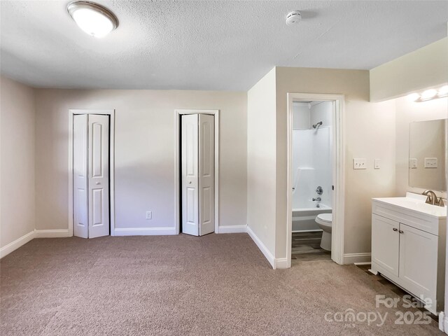 unfurnished bedroom with two closets, light carpet, a sink, a textured ceiling, and baseboards