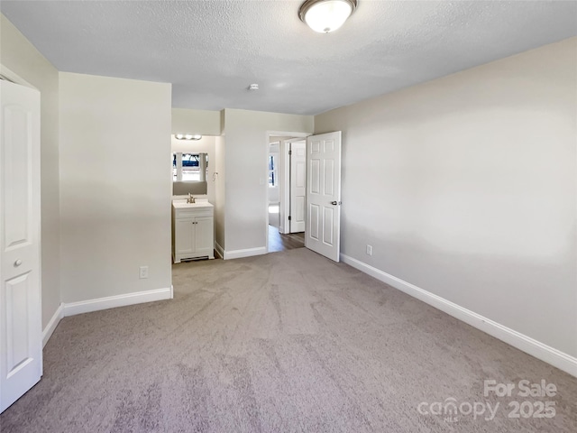 unfurnished bedroom with carpet flooring, connected bathroom, a sink, a textured ceiling, and baseboards