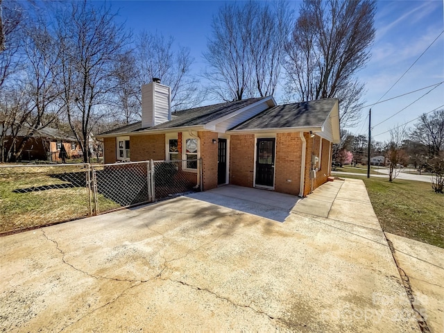 exterior space featuring driveway, brick siding, a chimney, and fence