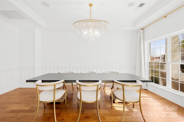 dining space featuring visible vents, a wainscoted wall, an inviting chandelier, light wood-style flooring, and ornamental molding