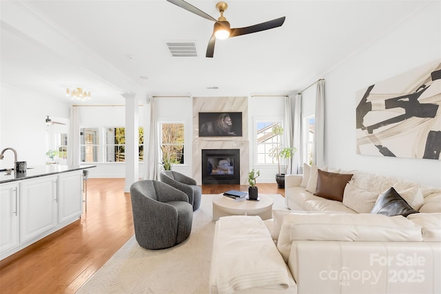 living room featuring visible vents, a fireplace, ceiling fan, ornamental molding, and light wood-type flooring