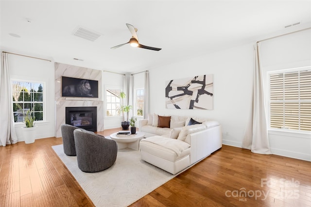 living room featuring a ceiling fan, wood finished floors, visible vents, and a high end fireplace