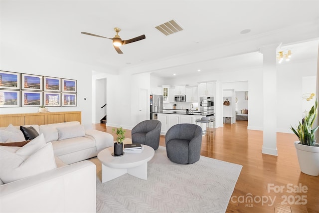 living area with stairway, baseboards, visible vents, light wood finished floors, and ceiling fan