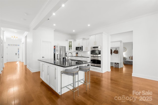 kitchen with dark countertops, light wood-type flooring, ornamental molding, stainless steel appliances, and a sink