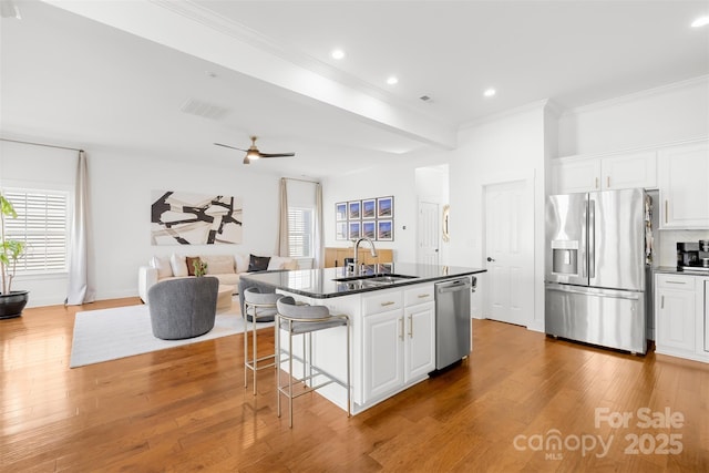 kitchen with wood finished floors, a sink, appliances with stainless steel finishes, dark countertops, and open floor plan