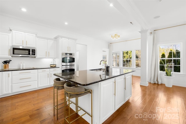 kitchen with light wood-type flooring, an island with sink, a sink, appliances with stainless steel finishes, and crown molding